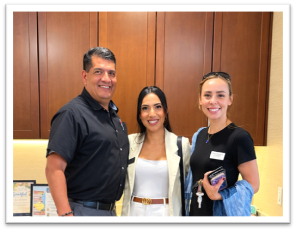 A man and two women smiling together in front of wooden cabinets.