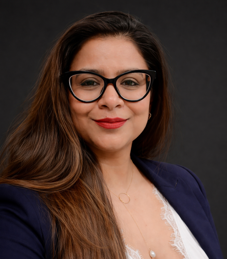 A woman with long hair and black-framed glasses smiles at the camera, wearing a navy blazer over a white top.